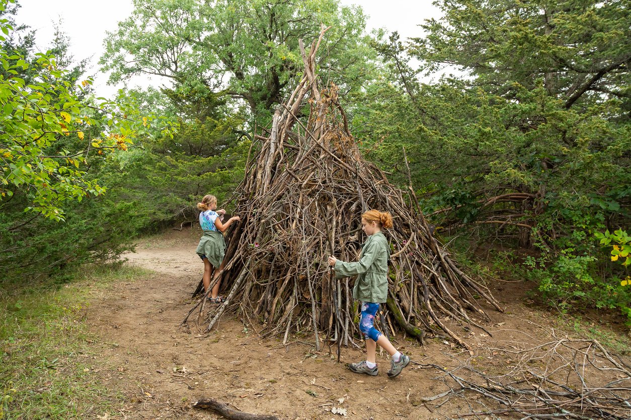Two Girls Helping Build Large Stick Fort in Woods