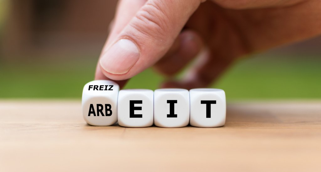 Hand turns a dice and changes the German word "Arbeit" ("work" in English) to "Freizeit" ("leisure time" in English).